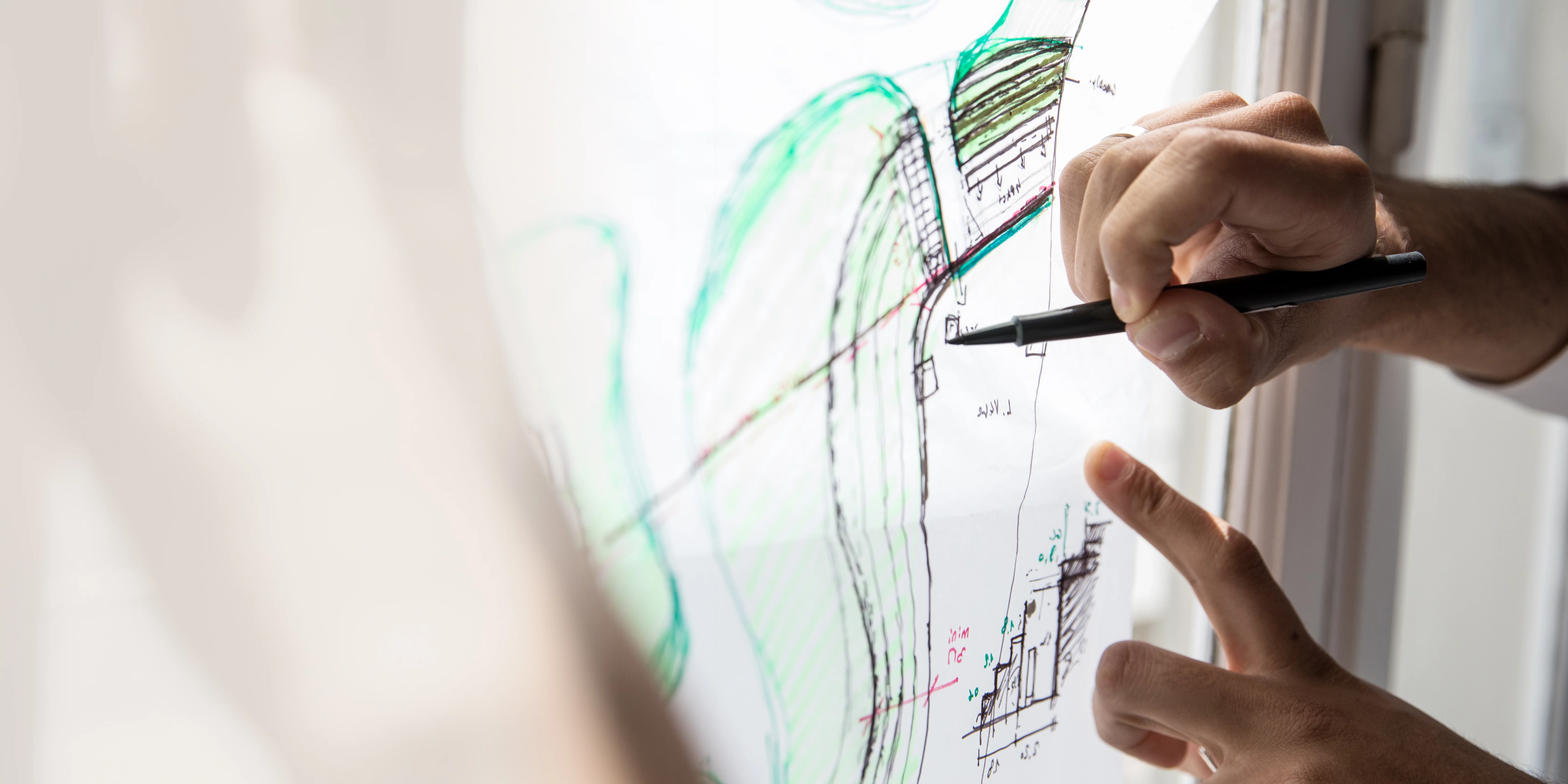 Hände zeichnen präzise auf einen transparenten Plan, der am Fenster befestigt ist