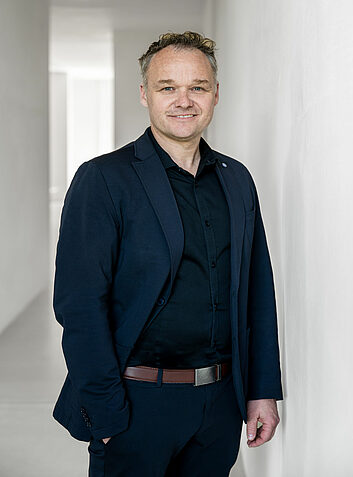 Smiling man with a dark jacket standing in a bright corner