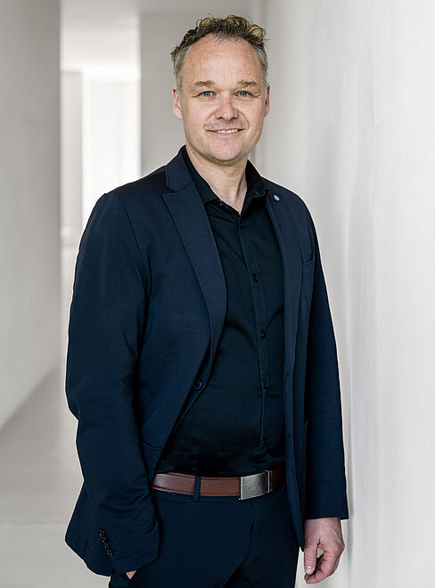 Mann in Anzug steht vor einer Wand in einem hellen Raum.