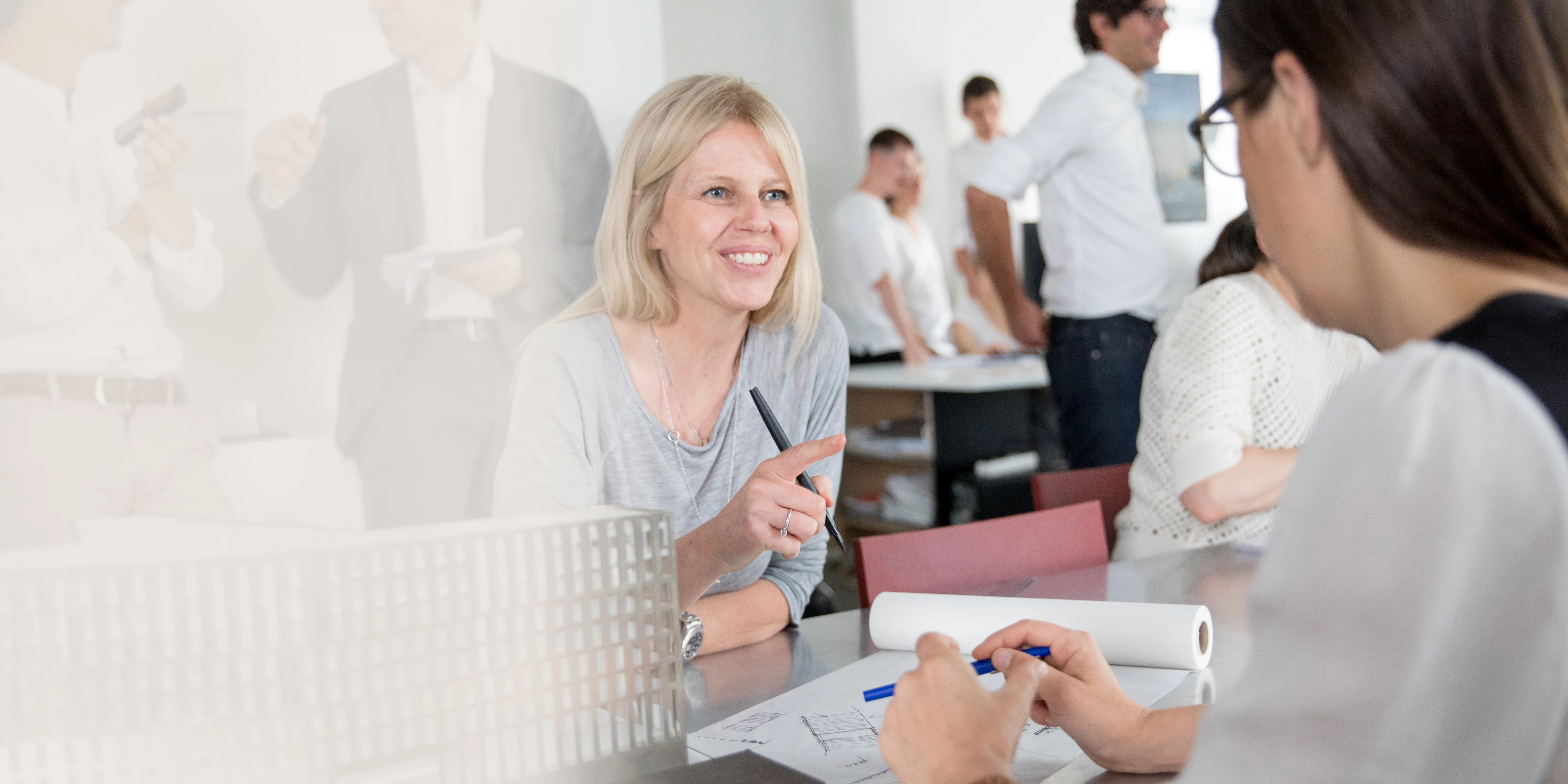 Architektinnen unterhalten sich freundlich im Büro über Architekturpläne und Modelle