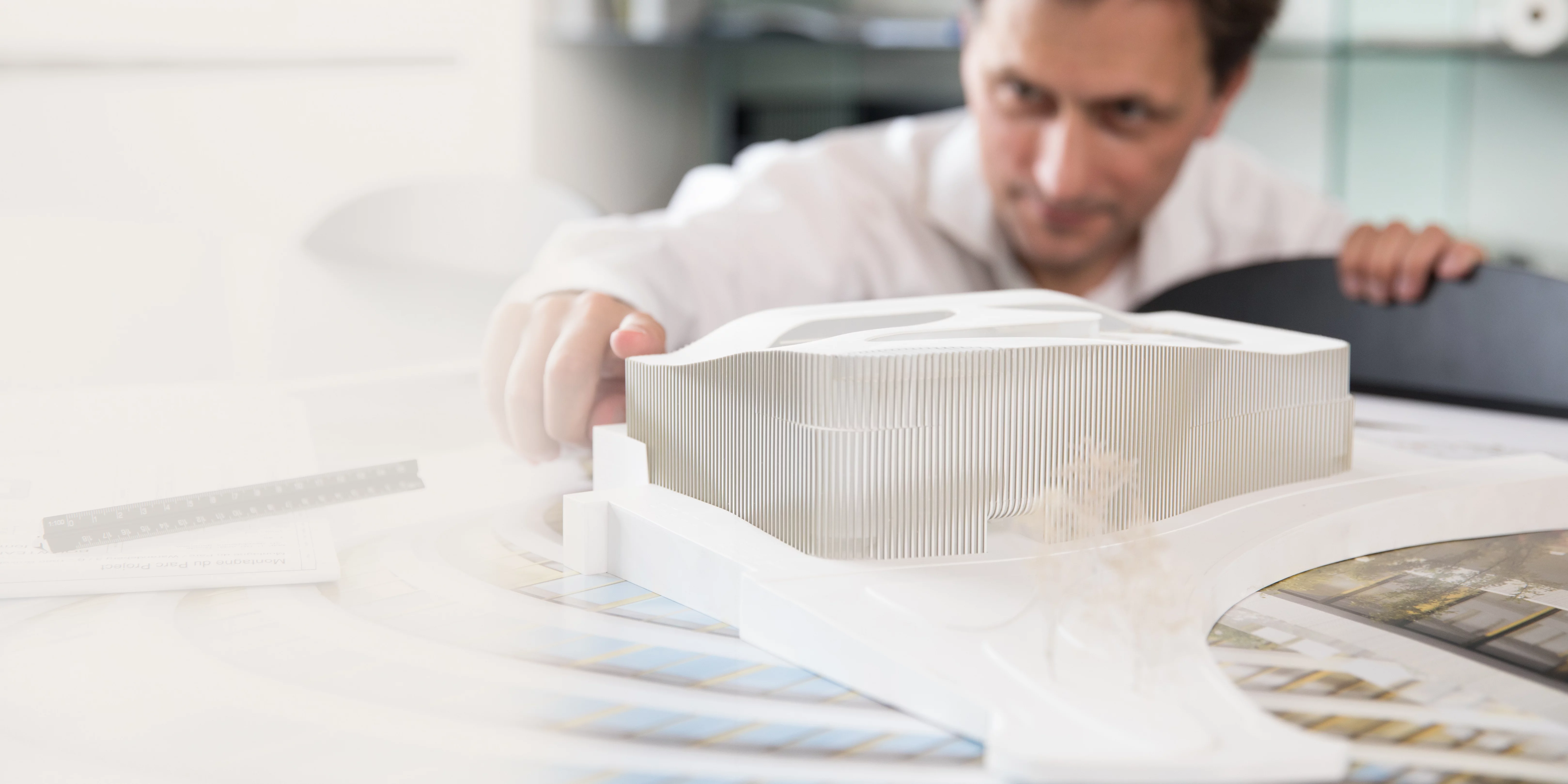 An architect works with concentration on a detailed architectural model at their desk