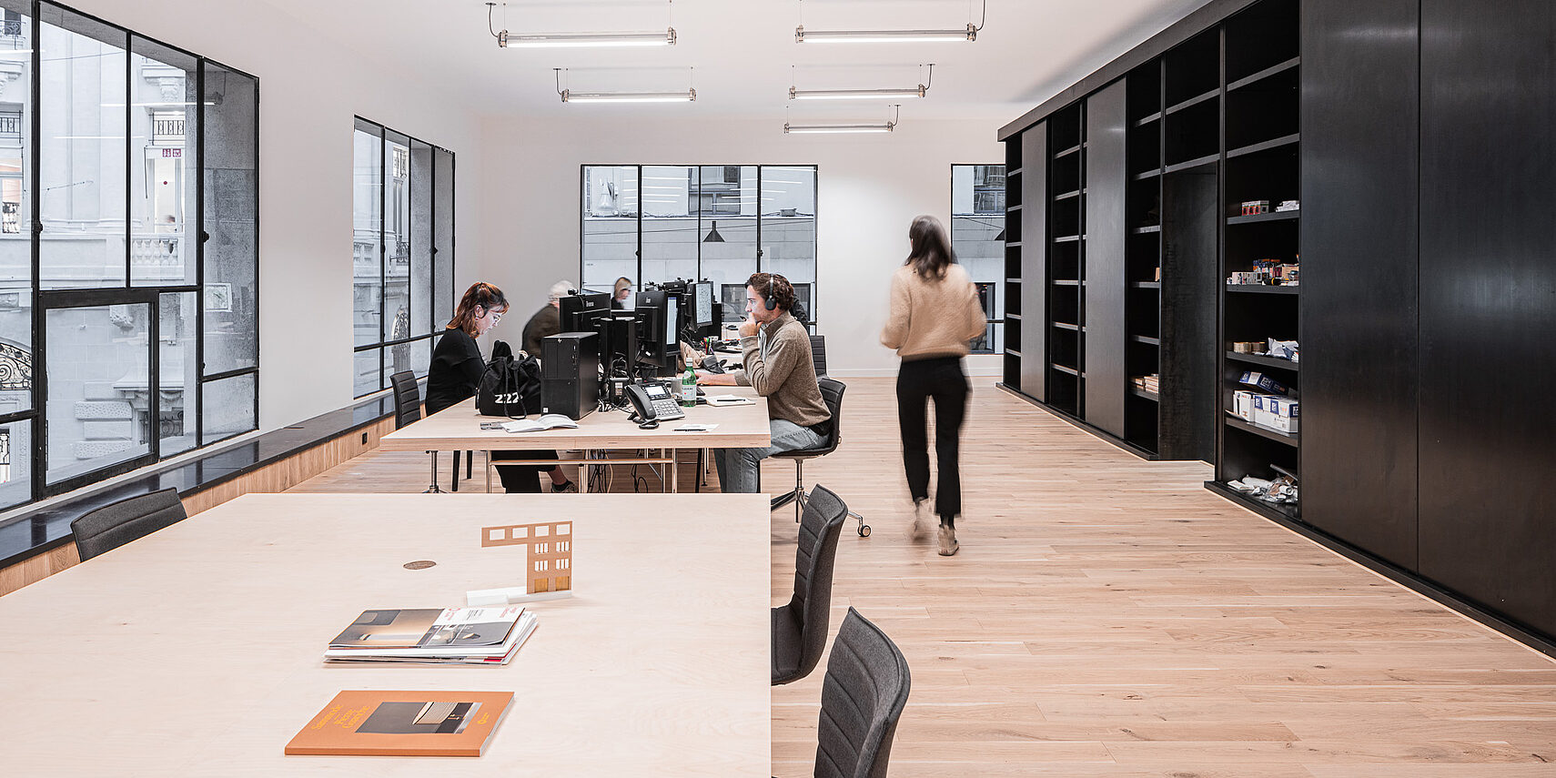 Büro mit mehreren Arbeitsplätzen, Computern, Tischen und Stühlen. Eine Person bewegt sich im Raum.
