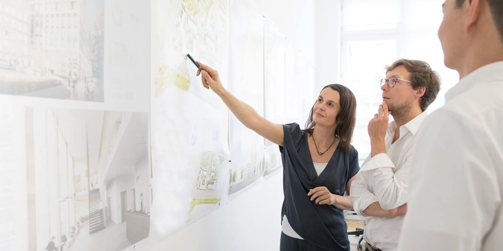 An architect presents plans on a wall and discusses the project with colleagues