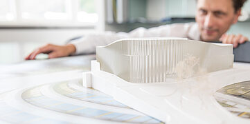 Ein Architekt betrachtet ein Architekturmodell auf einem Tisch, umgeben von Plänen und Zeichnungen.